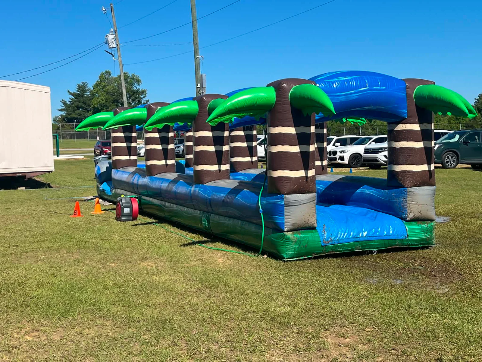 Wow Inflatables tropical palm tree inflatable slip-n-slide with four palm trees and dual racing lanes set up on green grass at outdoor summer event in Forsyth Georgia