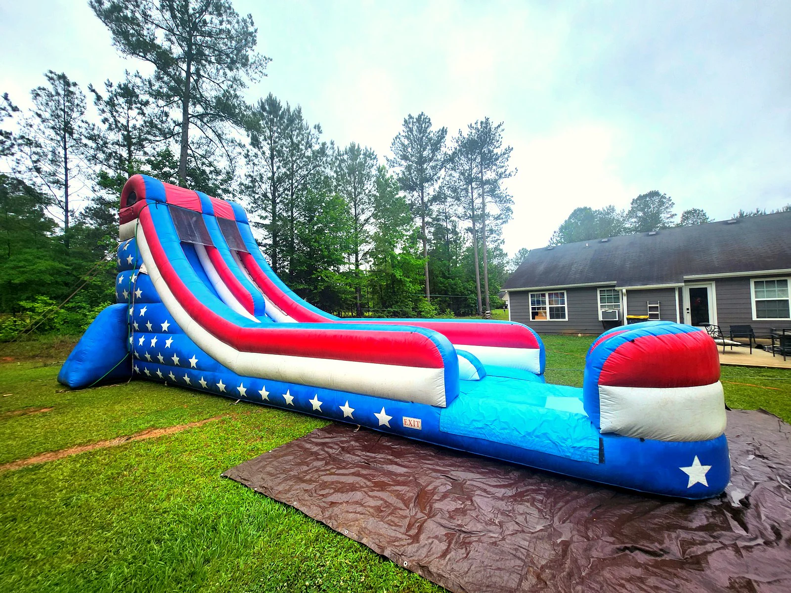 Wow Inflatables American flag themed inflatable water slide rental side view in Sharpsburg Georgia backyard — tall red white and blue water slide with white stars and long splash run at residential birthday party in Coweta County