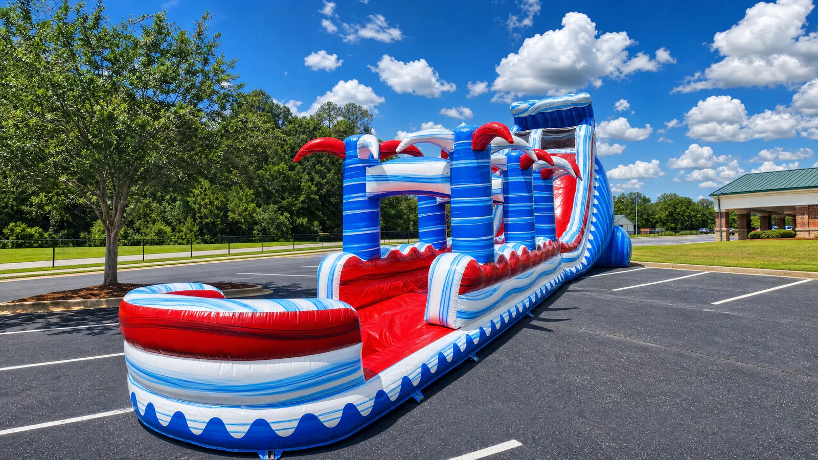 Wow Inflatables large blue red and white wave pattern inflatable water slide with red claw decorations and long slip section set up in commercial parking lot in Bonaire Georgia — large water slide rental Houston County