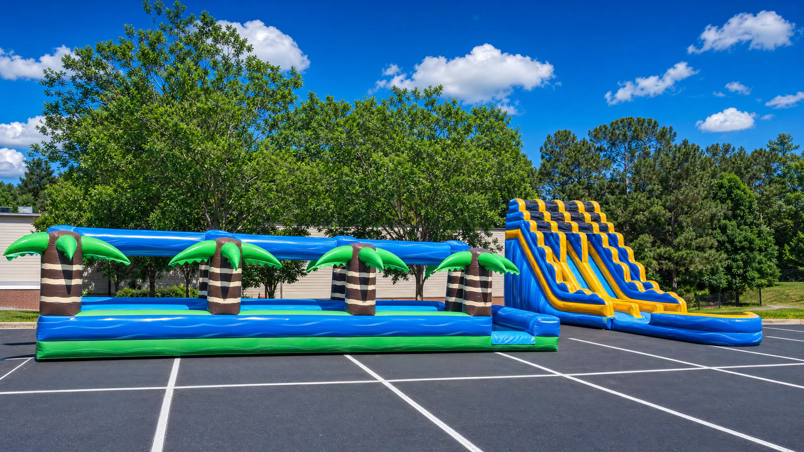 Wow Inflatables tropical palm tree slip-n-slide and tall blue yellow black water slide set up side by side in commercial parking lot in Macon Georgia — multi-unit inflatable rental Middle Georgia event