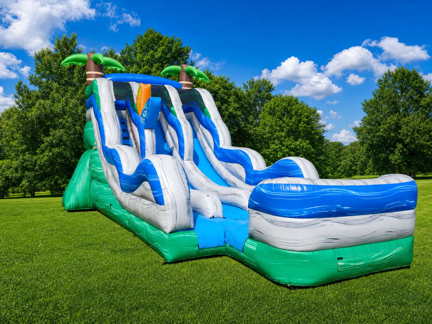 Wow Inflatables tropical dual-lane inflatable water slide with blue gray green wave patterns palm tree toppers and large splash pool set up on green grass in Forsyth Georgia — tropical water slide rental Monroe County