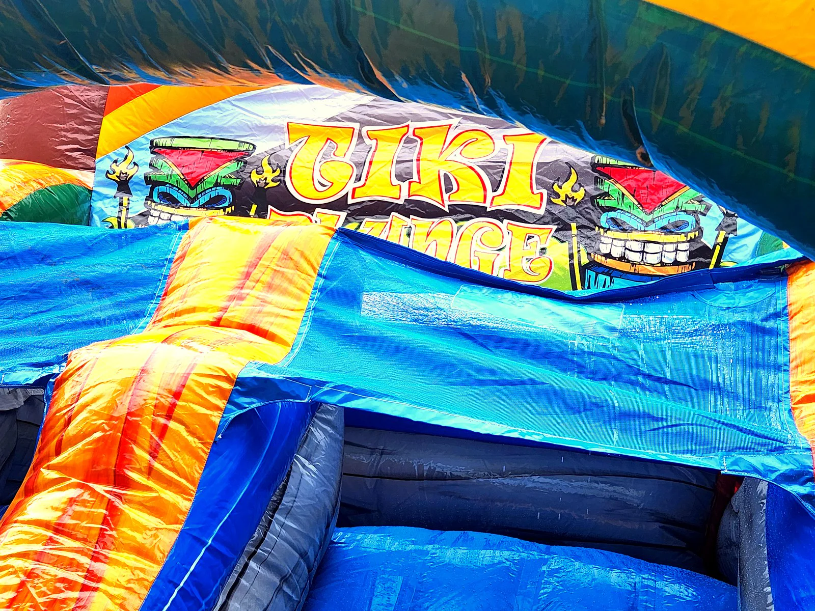 Close-up of Tiki Plunge inflatable water slide name banner at a Newman GA backyard party rental by Wow Inflatables — colorful tiki themed inflatable with orange blue and yellow panels