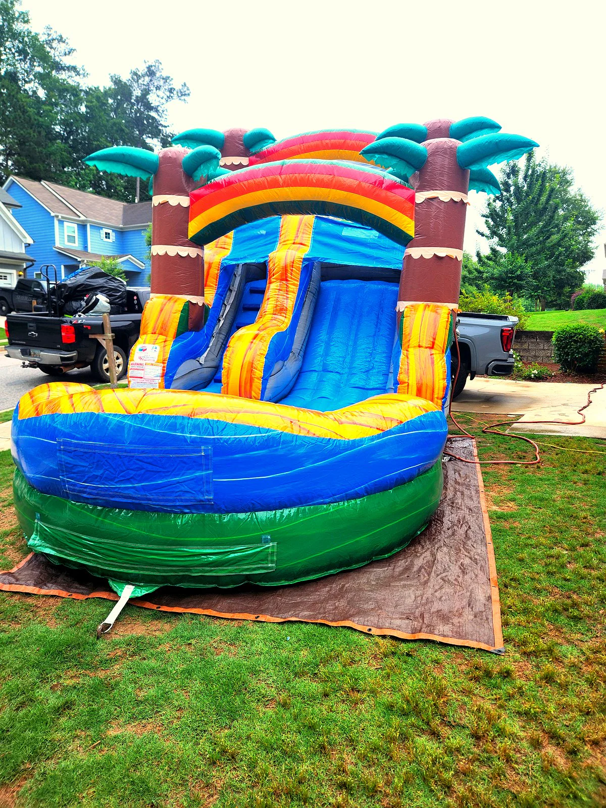 Wow Inflatables dual lane Tiki inflatable water slide rental in Newman Georgia neighborhood — tropical themed water slide with palm tree columns and large splash pool on green grass