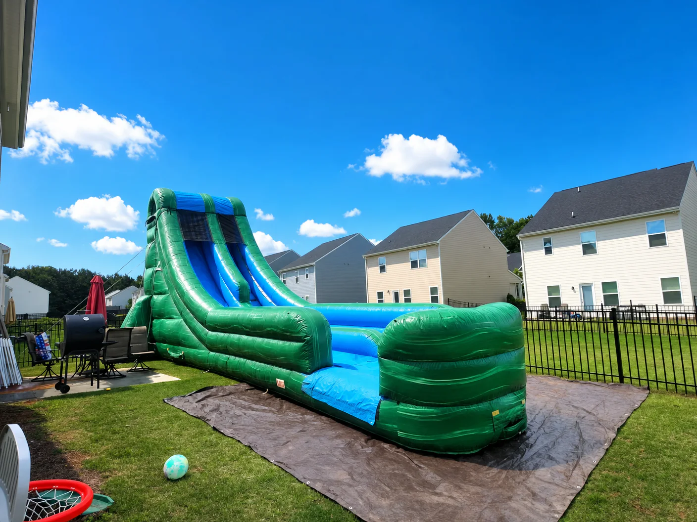 Wow Inflatables giant green and blue inflatable water slide rental set up in residential backyard in Georgia — tall dual-lane water slide with splash pool on green grass