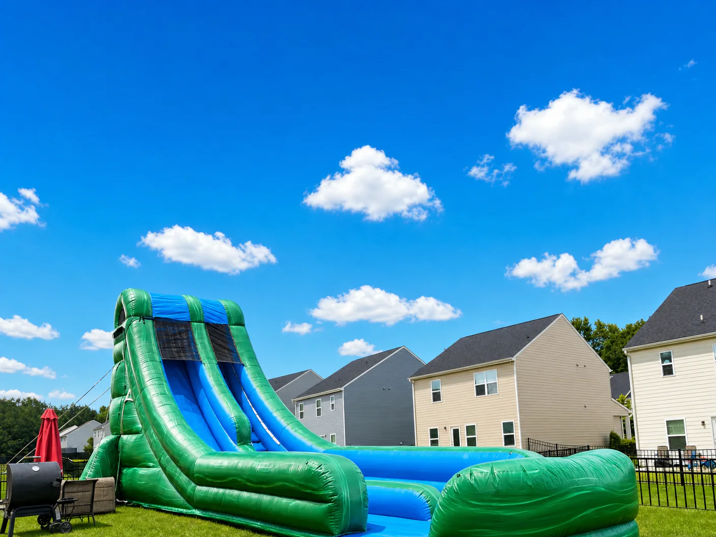 Wow Inflatables giant green inflatable water slide rental side view at backyard birthday party in Georgia — 20 foot tall water slide with blue splash pool and green grass