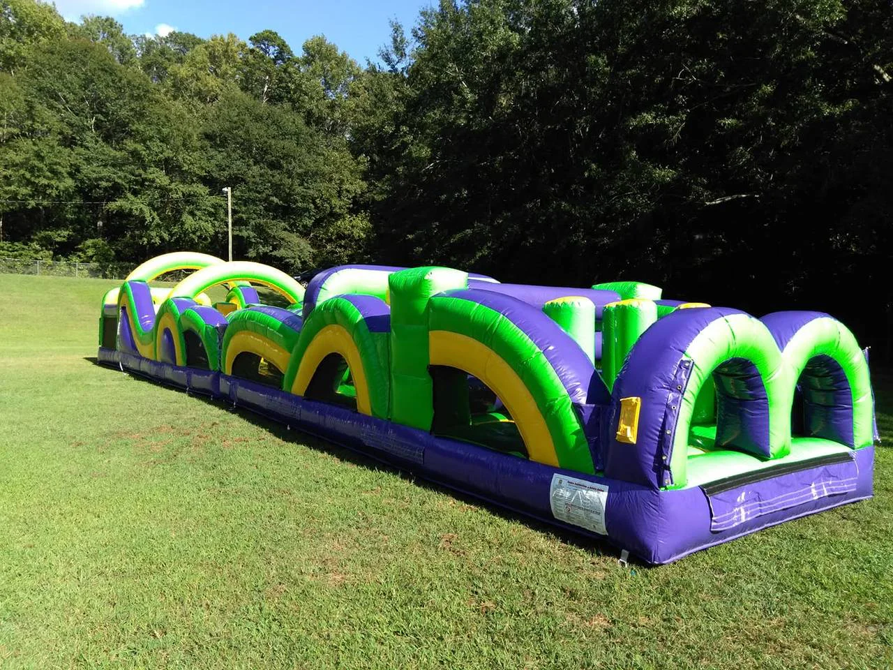 Wow Inflatables purple green and yellow inflatable obstacle course rental at outdoor event in Middle Georgia — long commercial-grade obstacle course for school and church events