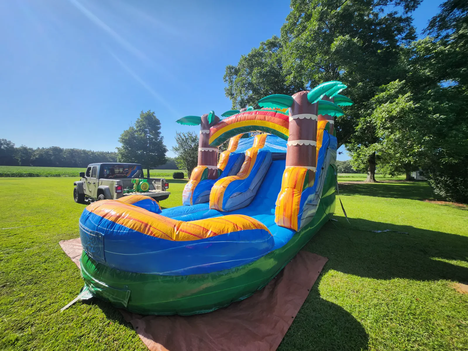 Wow Inflatables tropical palm tree dual-lane inflatable water slide rental in Forsyth Georgia — yellow blue and green tropical themed commercial water slide at outdoor event