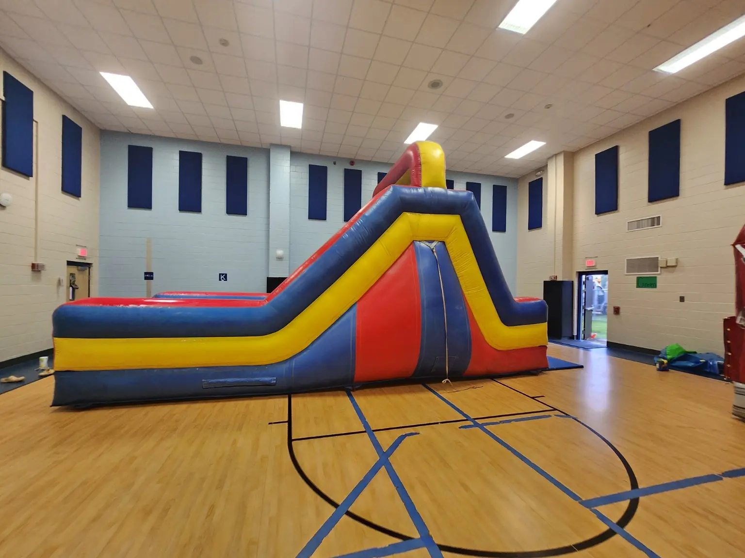 Red yellow and blue inflatable obstacle course slide set up inside a gymnasium