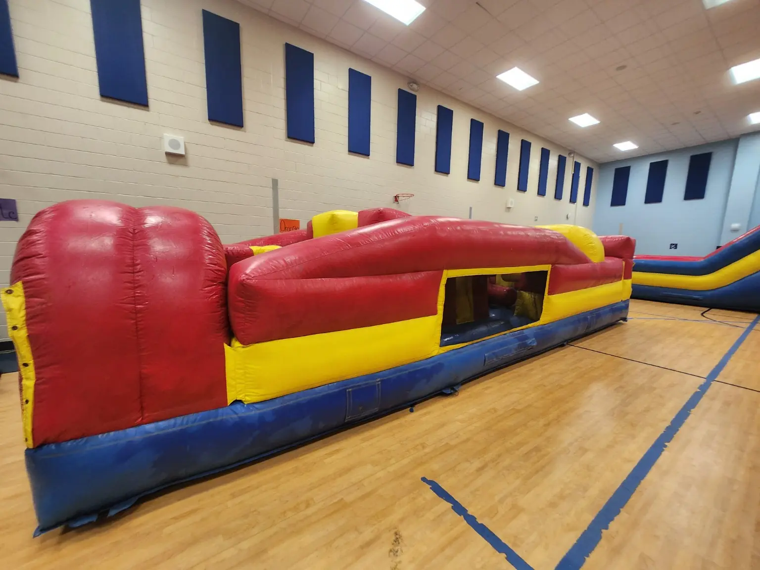 Side view of a red yellow and blue inflatable obstacle course set up inside a gymnasium