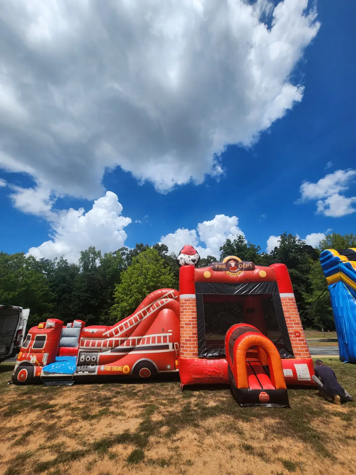 Red Fire House inflatable combo with a fire-engine side slide and front bounce-house entrance on grass